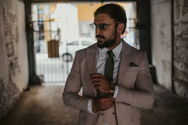 Man in suit fixing shirt button and standing in the building corridor on a sunny day