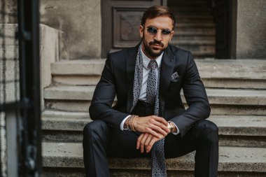 Merdivenlerde oturan ve bir fotoğraf makinesi ararken saatini holding ciddi iş adamı