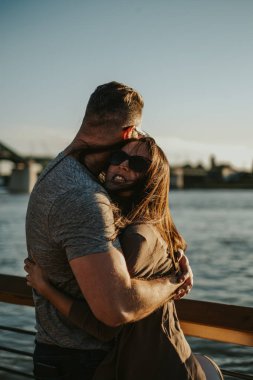 Eğleniyor ve nehir kıyısında günbatımında sarılma bir çift. Güzel bir güneşli gün