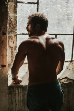 Sert, atletik, gömleksiz adam kızgın ifade ile pencerenin yanında ayakta