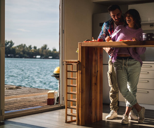 Couple in love, cutting vegetables in the kitchen with river view on a beautiful autumn day