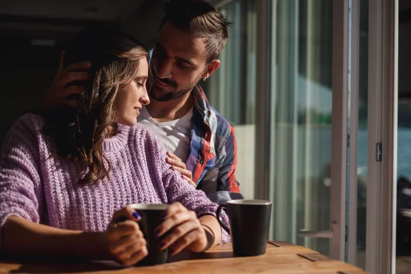 英俊的男人拥抱女朋友 而他们喝咖啡的窗口在一个美丽的阳光明媚的一天 — 图库照片