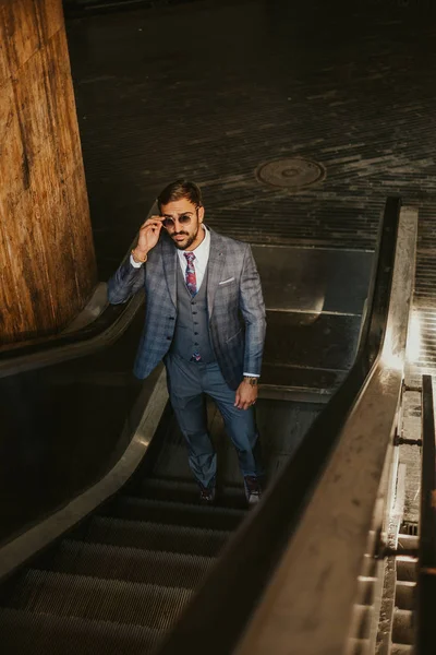 Hombre de negocios serio subiendo a la escalera mecánica mientras sostiene cantado — Foto de Stock