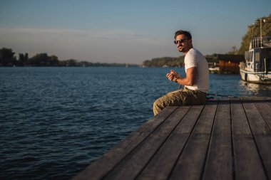 İskelede oturup ve güneşe bakarak adam