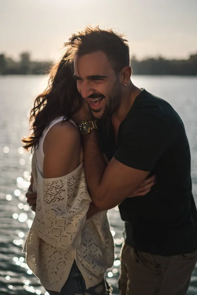 Boldog pár átölelte és nevetett a folyó partján naplementében — Stock Fotó