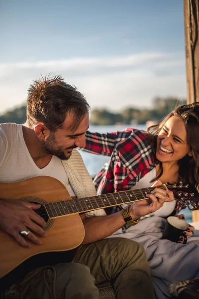 Çift gülüyor ve nehrin yanında gitar çalmak — Stok fotoğraf