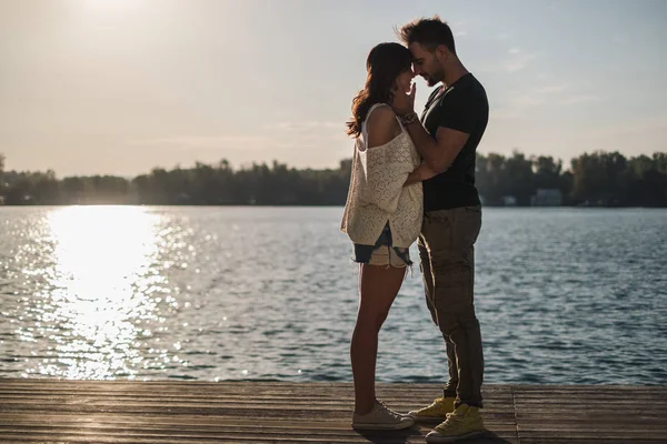 Coppia innamorata che tocca le teste lungo il fiume al tramonto — Foto Stock