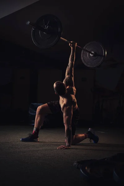 Wytatuowany sportowiec trzyma wagi przez głowę jedną ręką — Zdjęcie stockowe