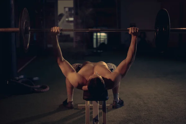 Un hombre sin camisa haciendo press de banca en el gimnasio —  Fotos de Stock