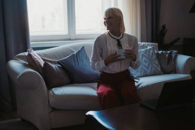 Pencere kenarındaki kanepede kahve içme gülümseyen kız