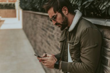 Sinirli, şık, sakallı bir adam cep telefonuyla mesaj atıyor.