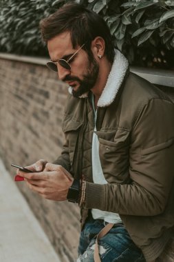 Sinirli, şehirli, sakallı bir adam cep telefonunda yazıyor.