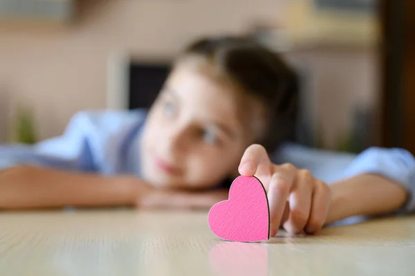 A small heart in a girl\'s hand. The girl looks out the window. Focusing on the heart.