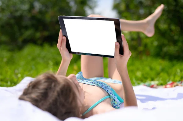 青い水着の女の子が庭で日光浴をしていて タブレットを持っています 白いディスプレイが付いているタブレット 休暇中にガジェットを通信し 使用するアイデア — ストック写真