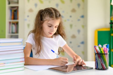 Kız ödevini yapıyor ve tableti kullanıyor. Kız öğrenci oturur.