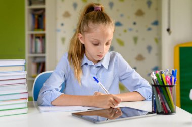 Kız interneti kullanarak yazılı dersler alıyor. Masanın üstünde. 