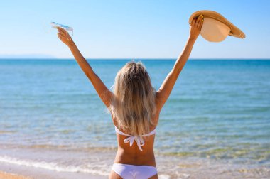 A girl in a white bathing suit stands by the sea with her arms r clipart