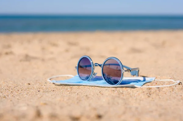 Óculos Sol Sobre Uma Máscara Médica Praia Areia Contra — Fotografia de Stock