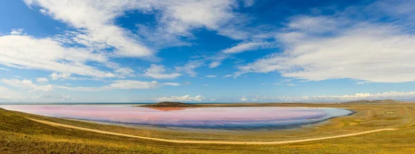 View of a small pink lake. Around the lake fields. above the lake blue sky with clouds.