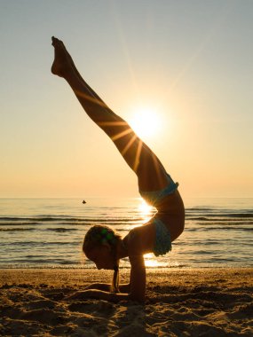 Sahilde bir jimnastikçi amuda kalkar. Ayakların yanında batan güneşten gelen güzel bir parıltı var..