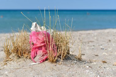 Garbage on the beach against the background of the sea. A pink bag and a syringe lie on the beach. clipart