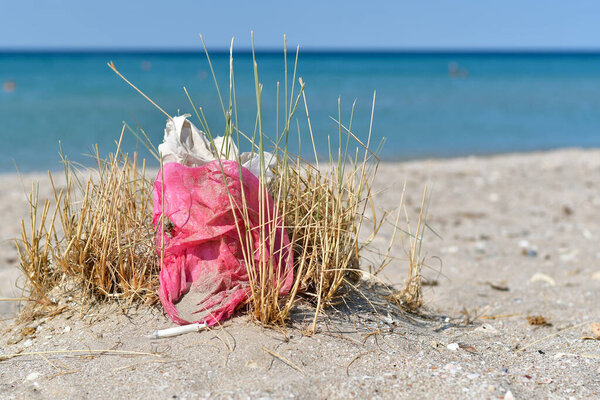 Garbage on the beach against the background of the sea. A pink bag and a syringe lie on the beach.