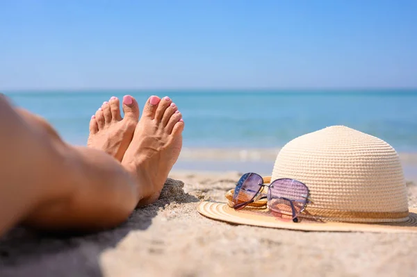 海を背景に少女の足 近くには麦藁帽子とサングラスがあります 海による休日の概念 — ストック写真