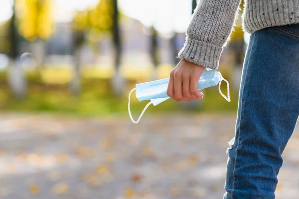 Sonbahar parkının arka planında bir gencin elindeki tıbbi maske. Coronavirüs sırasında tıbbi maske kullanımı kavramı.