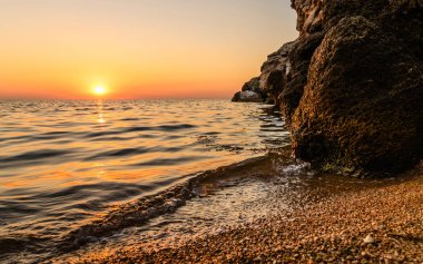 Gün batımında kıyıda. Deniz kenarındaki büyük siyah taşlar. Akşamları deniz manzarası