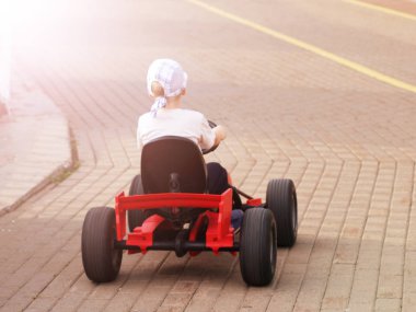 Parkta, arka görüş bir araba sürme bir kap içinde küçük bir çocuk. Arabada pedallar. Günbatımı.