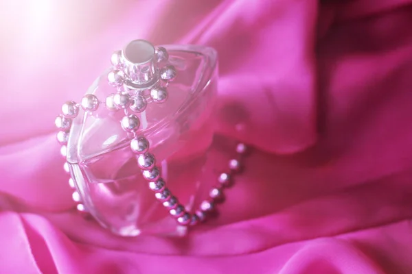 Garrafa de perfume e contas sobre vestido rosa Imagem De Stock