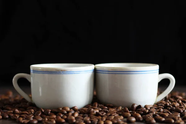 Czarna kawa w białych kubkach i ziaren kawy na czarnym tle. — Zdjęcie stockowe