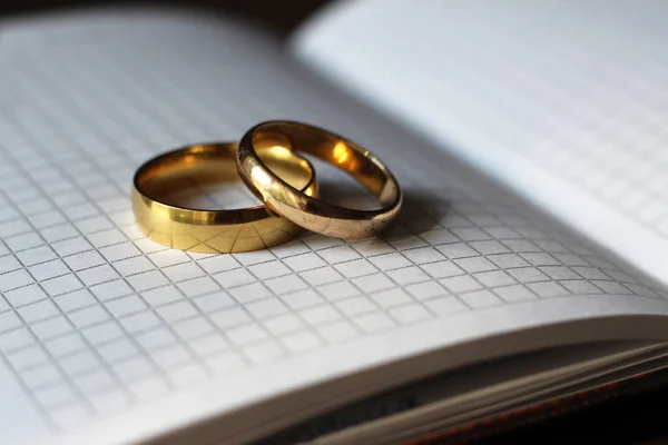 Dois anéis de casamento de ouro e um caderno de papel — Fotografia de Stock