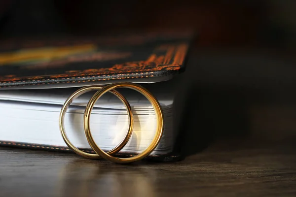 Two gold wedding rings and a paper notebook, wooden table — Stock Photo, Image