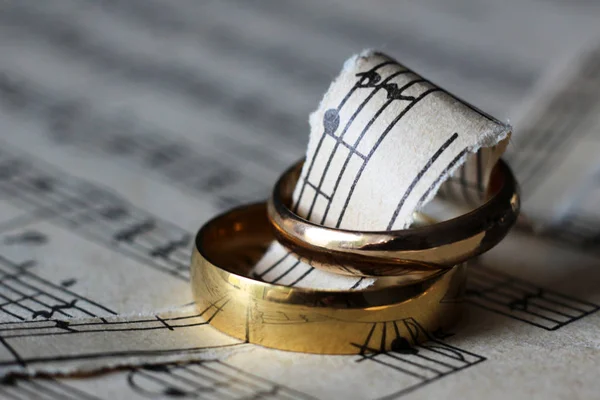 Two wedding rings and old musical notes — Stock Photo, Image