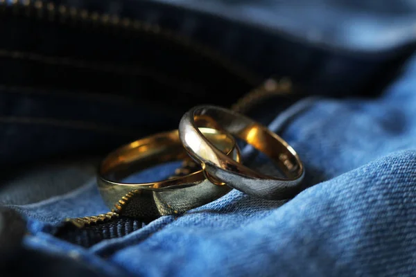 蓝色牛仔裤上的两枚金色结婚戒指。爱情或婚姻的概念. — 图库照片