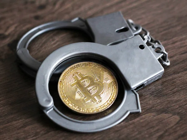 Altın bitcoin ve kelepçe ahşap bir masa, siber suç.