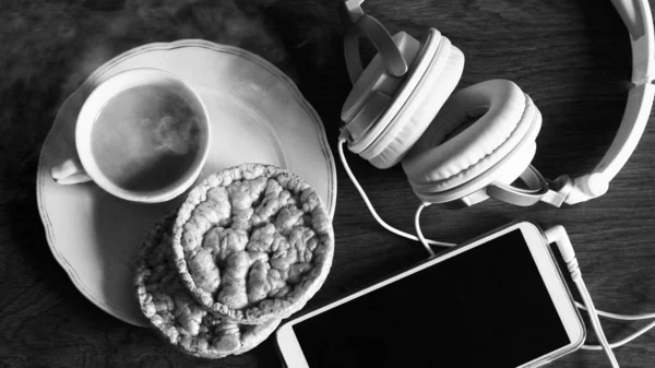 Coffee cup and fresh baked croissants, earphones, smart phone on wooden background. Top View. Black and white.