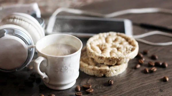 コーヒーと丸いパン、大きな白いヘッドフォン、木製のテーブルの上のスマートフォン — ストック写真
