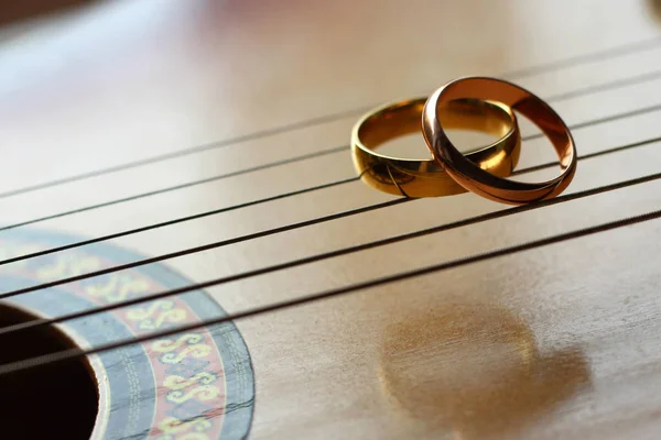 Dois anéis de casamento de ouro mentira em cordas de guitarra close-up — Fotografia de Stock