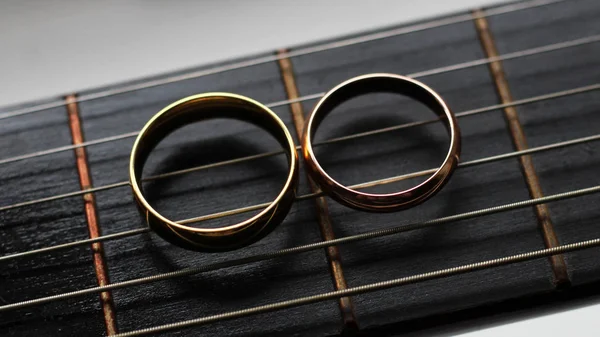 Dois anéis de casamento de ouro mentira em cordas de guitarra close-up — Fotografia de Stock