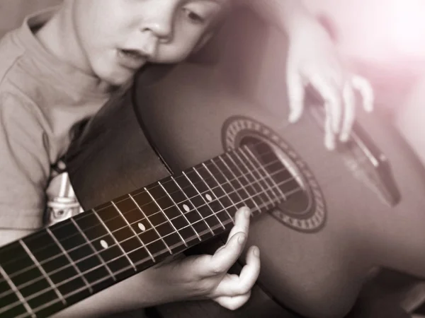 Malý chlapec hraje doma na kytaru tak blízko, černobíle — Stock fotografie