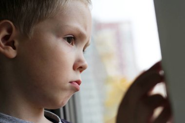 Sarışın çocuk üzgün ve pencereden dışarı bakıyor.