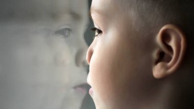 Pencereden bakan küçük çocuk. Camdaki yüzün yansıması..