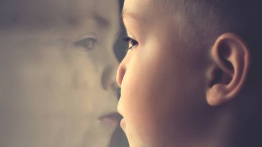 Pencereden bakan küçük çocuk. Bardaktaki yüzün yansıması. Klasik tonlu.