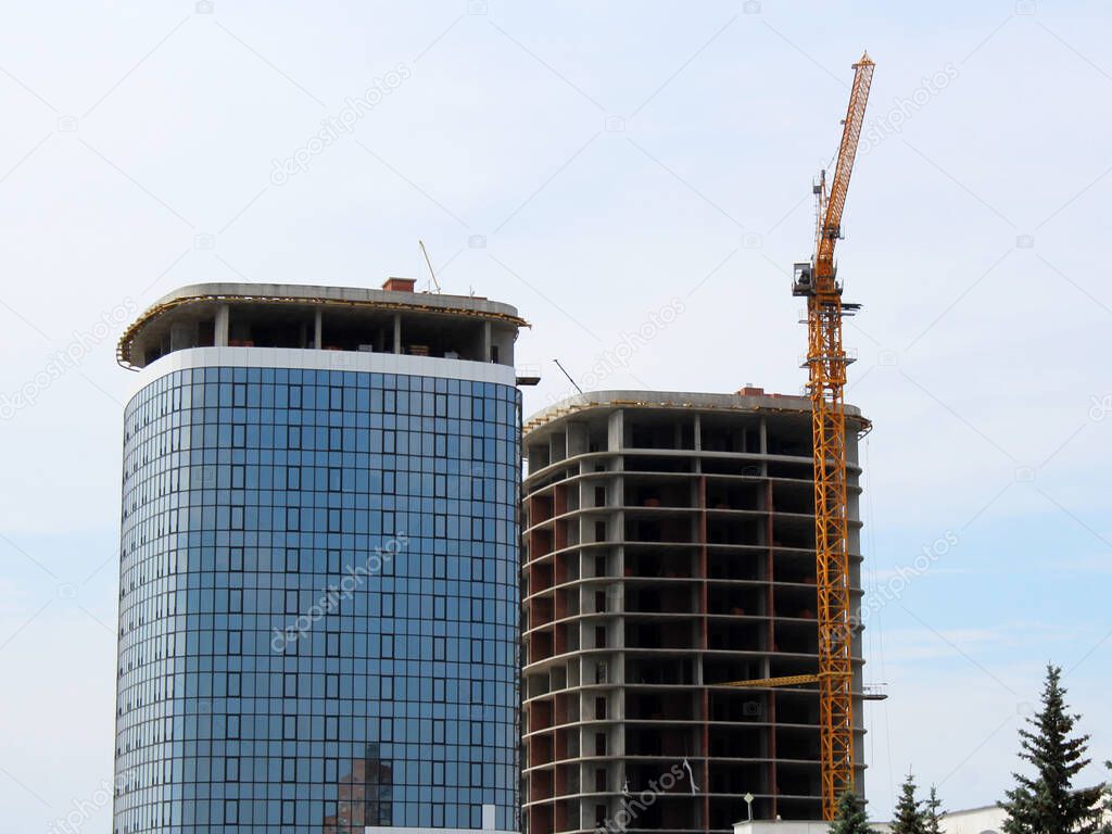Photos of high-rise construction cranes and unfinished house against the blue sky with clouds. Taken from the bottom up