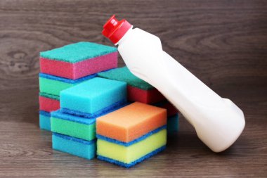 Renkli mutfak süngeri ve bir şişe bulaşık deterjanı, ahşap arka plan.
