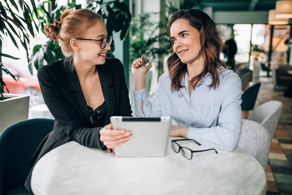 Two girls at a business meeting in a cafe. Drink coffee. Discuss future corporations and its projects. Sign a contract. Red-haired girl and brunette.