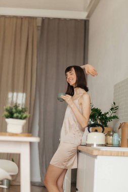 Mutfakta pijamalarıyla gülümseyen bir kız. Güneşli sabahla tanışır. Lezzetli kahve hazırlar.