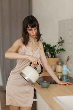 Mutfakta pijamalarıyla gülümseyen bir kız. Güneşli sabahla tanışır. Lezzetli kahve hazırlar.